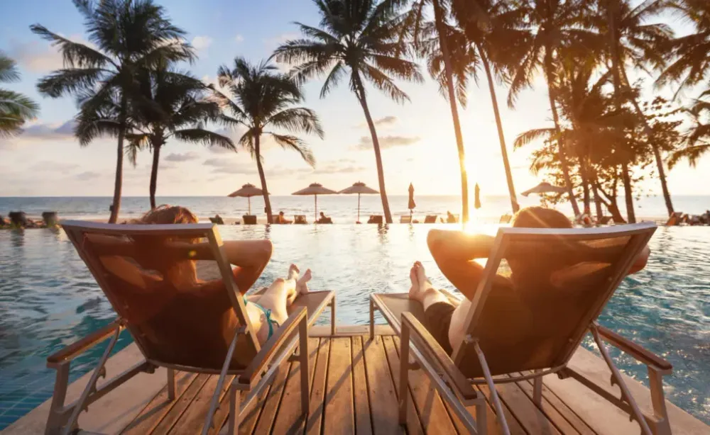 Two people relaxing on beach chairs in front of a pool at sunset